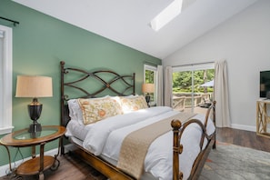 A bedroom with a bed, two bedside tables, a TV, and a balcony with outdoor furniture.
