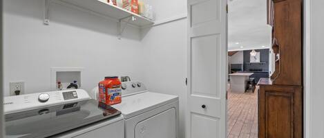 A laundry area with a front-loading washer and dryer, a shelf with cleaning supplies, and a wooden cabinet.