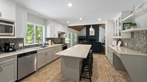 A modern kitchen with granite countertops, stainless steel appliances, and a central island with bar stools. - Beautiful Colonial Home in Saunderstown, RI (North Kingstown)