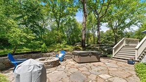 A stone patio with outdoor furniture, a covered grill, and a fire pit. - Beautiful Colonial Home in Saunderstown, RI (North Kingstown)