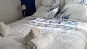 A neatly made bed with floral-patterned bedding and two rolled towels. - Cottage T2 (Lit-et-Mixe)