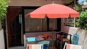 A patio with two striped lounge chairs, a table with a red umbrella, and a dining setup. - Cottage T2 (Lit-et-Mixe)