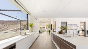 A modern kitchen with a large island, a built-in oven, and a view of the desert landscape. - The Dream House - A Desert Masterpiece with Infinity Pool and Sauna (Palm Desert)