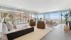 A modern living room with a large bed, two armchairs, and a view of a rocky landscape through large windows. - The Dream House - A Desert Masterpiece with Infinity Pool and Sauna (Palm Desert)