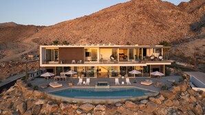 A modern two-story house with a swimming pool, outdoor seating, and a mountainous backdrop. - The Dream House - A Desert Masterpiece with Infinity Pool and Sauna (Palm Desert)