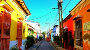 A narrow street lined with colorful buildings, a clear sky, and power lines. - 3G1-2 APARTAMENTO EN CARTAGENA (Cartagena)