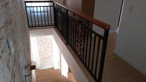 Uma escada de madeira com corrimão de metal preto, que dá acesso a um patamar.