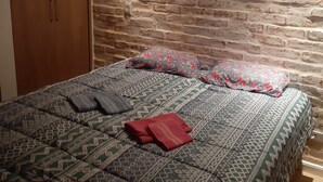 Quarto com cabeceira em padrão de tijolos, cama com roupa de cama estampada e guarda-roupa de madeira.