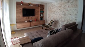 Sala de estar com unidade de entretenimento em madeira, TV de tela plana, sofá e poltrona estampada.