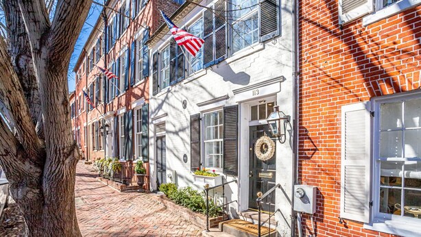 A brick building with a white facade, numbered 113, featuring a front entrance with steps and a small porch area.