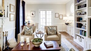 A well-lit living room with two armchairs, a coffee table with a bowl of green balls, a fireplace with candles, and a bookshelf.