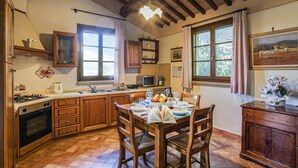 A kitchen with wooden cabinets, a dining table with chairs, a stove, and a window with curtains. - Casa Rialdo - Small family villa with private pool (Montecatini Val di Cecina)
