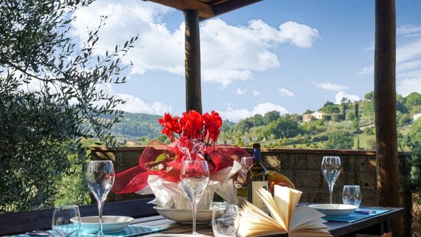 An outdoor dining table with wine glasses, a bowl, and an open book, set against a scenic hillside backdrop. - Casa Rialdo - Small family villa with private pool (Montecatini Val di Cecina)