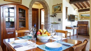 A dining area with a wooden table set for two, a fruit bowl, and a wine bottle. - Casa Rialdo - Small family villa with private pool (Montecatini Val di Cecina)