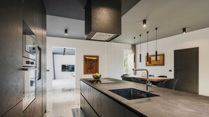 A modern kitchen with a central island, a dining area, and a view into the living space. - Modern villa for 6 guests with pool, surrounded by pine forest, near beach (Valica)