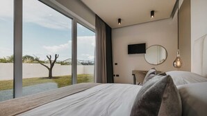 A modern hotel room with a large window, a flat-screen TV, a round mirror, and a bed with white linens. - Modern villa for 6 guests with pool, surrounded by pine forest, near beach (Valica)