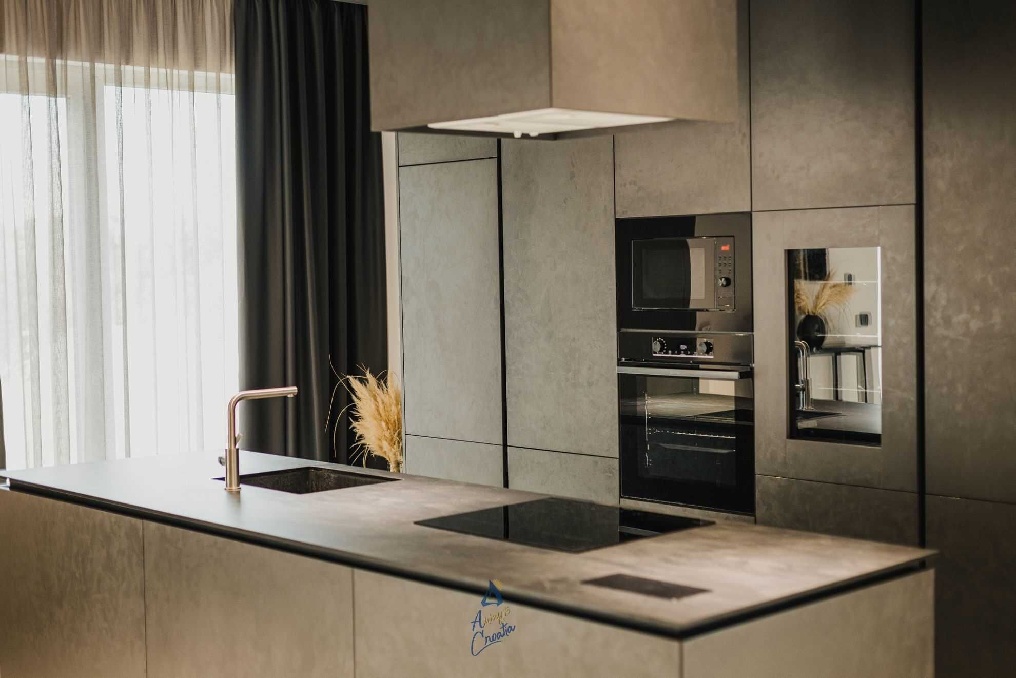 Una cocina moderna con una isla central, horno integrado y un amplio ventanal con cortinas.