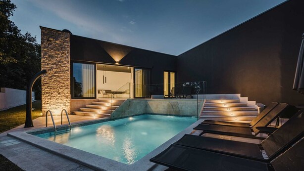 A modern outdoor pool area with a stone wall, a glass door leading to a balcony, and a set of stairs with outdoor seating. - Modern villa for 6 guests with pool, surrounded by pine forest, near beach (Valica)