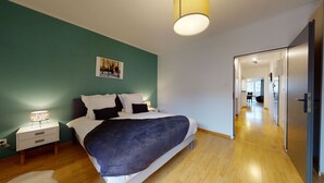 A bedroom with a bed, bedside table, lamp, and a painting on the wall. - le nid cosy 1 free garage  up to 2 (Colmar)