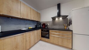A modern kitchen with wooden cabinets, a black countertop, a stainless steel range hood, a built-in oven, and a white refrigerator. - le nid cosy 1 free garage  up to 2 (Colmar)