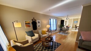 A modern living room with a sofa, armchair, and coffee table. There is a dining area in the background with a table and chairs.