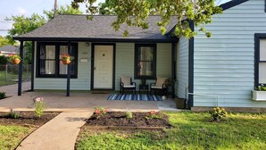 A small, light blue house with a porch, a door marked '120', and a small garden area with flowers and a pathway.