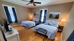 A hotel room with two beds, a desk, a chair, a ceiling fan, and a view of the ocean.