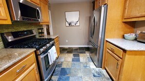 A kitchen with wooden cabinets, a stainless steel refrigerator, a microwave, a stove, and a tiled floor.