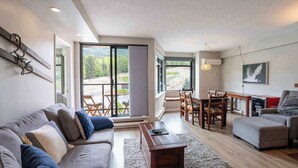 A modern living room with a sofa, ottoman, dining table, chairs, and a large sliding glass door leading to a balcony.