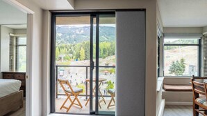 A room with a large sliding glass door leading to a balcony with outdoor seating and a mountain view.