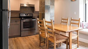A modern kitchen with stainless steel appliances, a stone accent wall, and a wooden dining table with chairs. - The Rainbow Suite Mountain and Village View (Whistler)