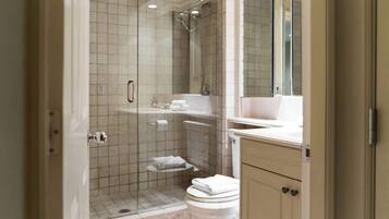 A bathroom with a glass-enclosed shower, a toilet, and a sink with a mirror above.