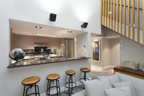 Una cocina moderna con una isla central, taburetes de bar y una zona de estar con sofá y cojines.
