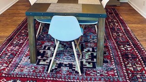 Comedor con mesa de madera, sillas blancas, alfombra estampada y candelabro.