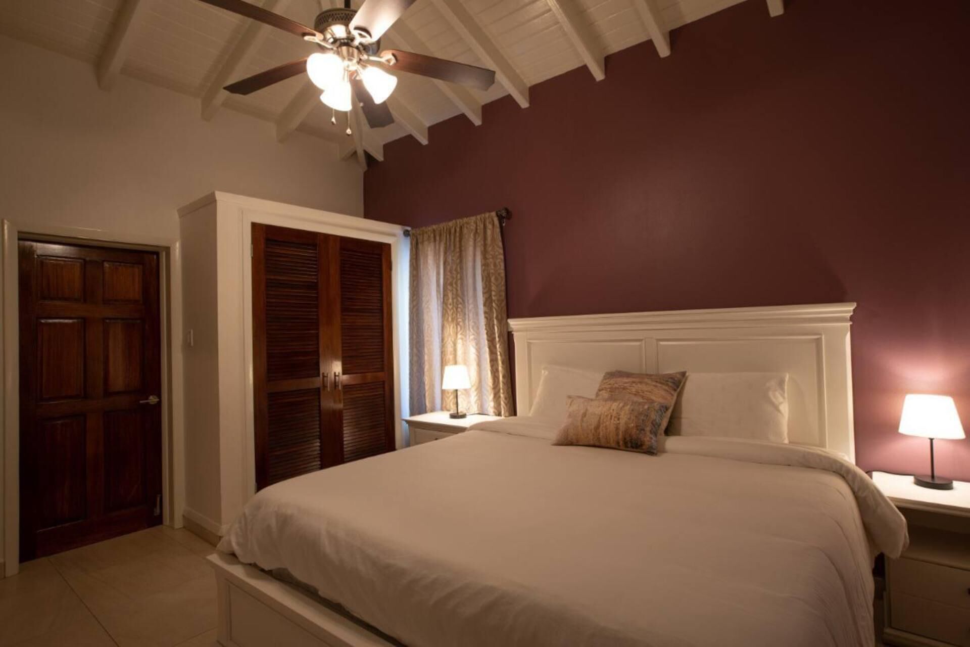 Une chambre à coucher comprenant un lit, des tables de chevet, un ventilateur de plafond et une armoire.