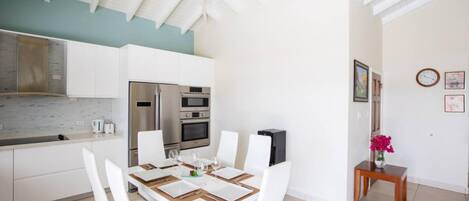A modern kitchen with white cabinets, stainless steel appliances, and a dining area with a white table and chairs.