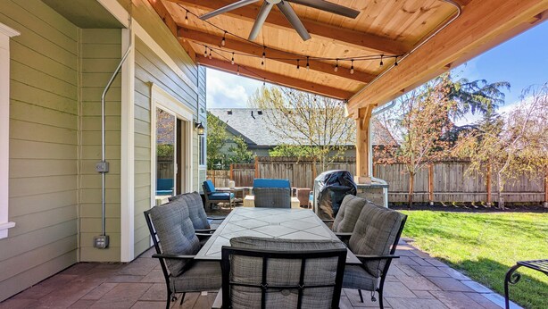 A covered patio with a table and chairs, a ceiling fan, and a wooden fence in the background.