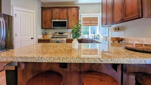 A kitchen with granite countertops, wooden cabinets, stainless steel appliances, and a central island with stools.