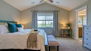 A bedroom with a bed, a bench, a nightstand, a ceiling fan, and a window with curtains.