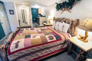 A bedroom with a large bed, a wooden headboard, a nightstand with a lamp, and a view of the bathroom.
