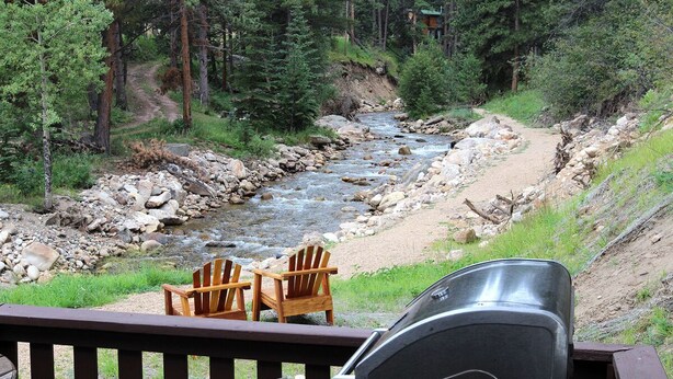 Una terraza con una parrilla y dos sillas Adirondack con vistas al río.