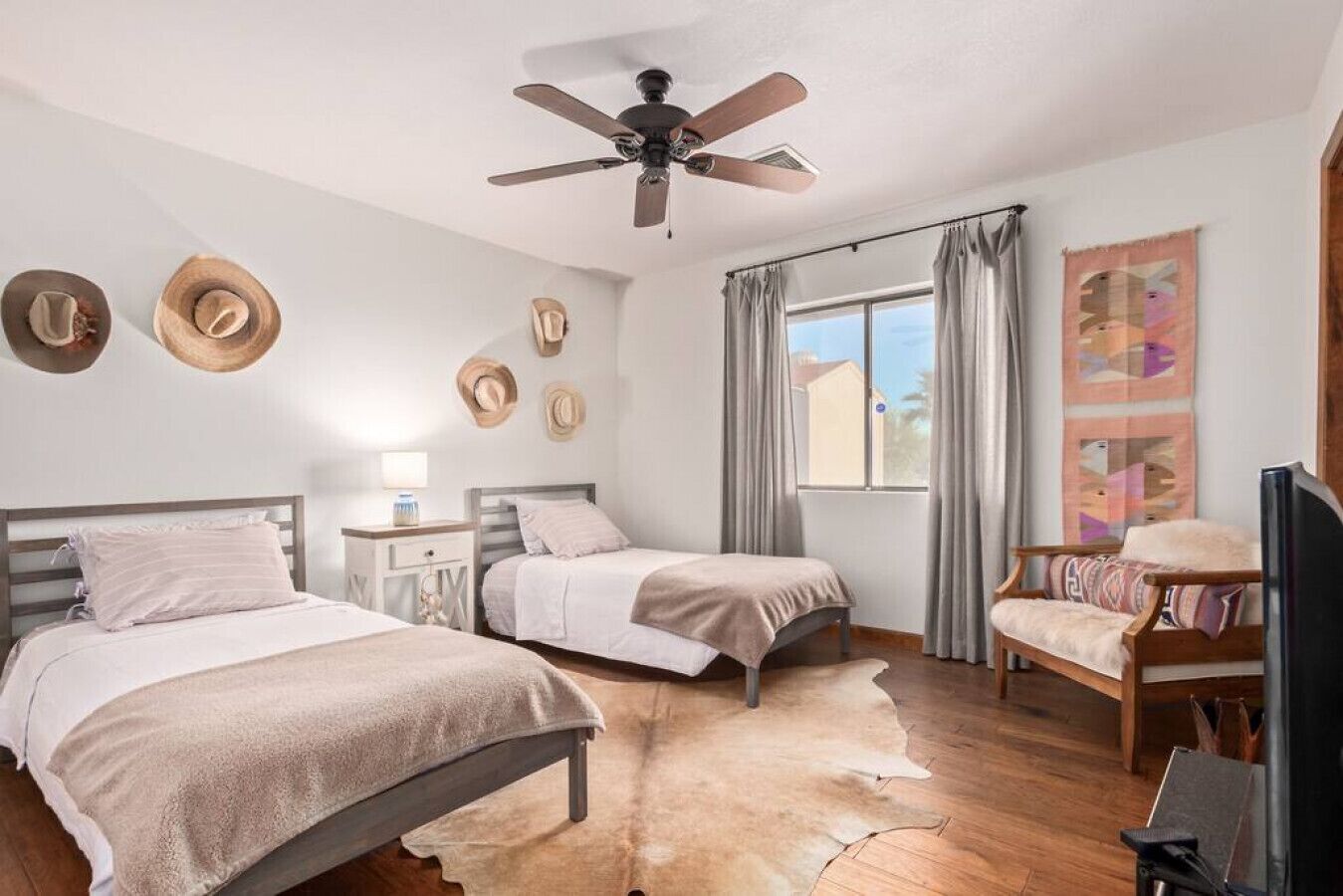 Una camera da letto con due letti, un ventilatore a soffitto, una finestra con tende e una sedia.