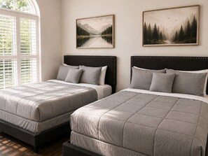Une chambre à coucher avec deux lits, chacun doté d’une tête de lit et d’oreillers, et deux tableaux représentant des paysages, encadrés et accrochés au mur.