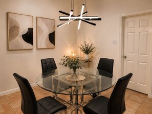 Un coin repas avec une table en verre entourée de chaises, un luminaire suspendu moderne et deux tableaux abstraits accrochés au mur.