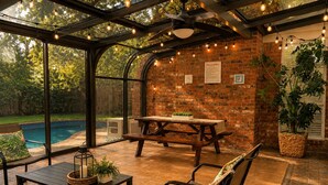 Un espacio de patio techado con pared de ladrillo, piscina y mobiliario exterior.