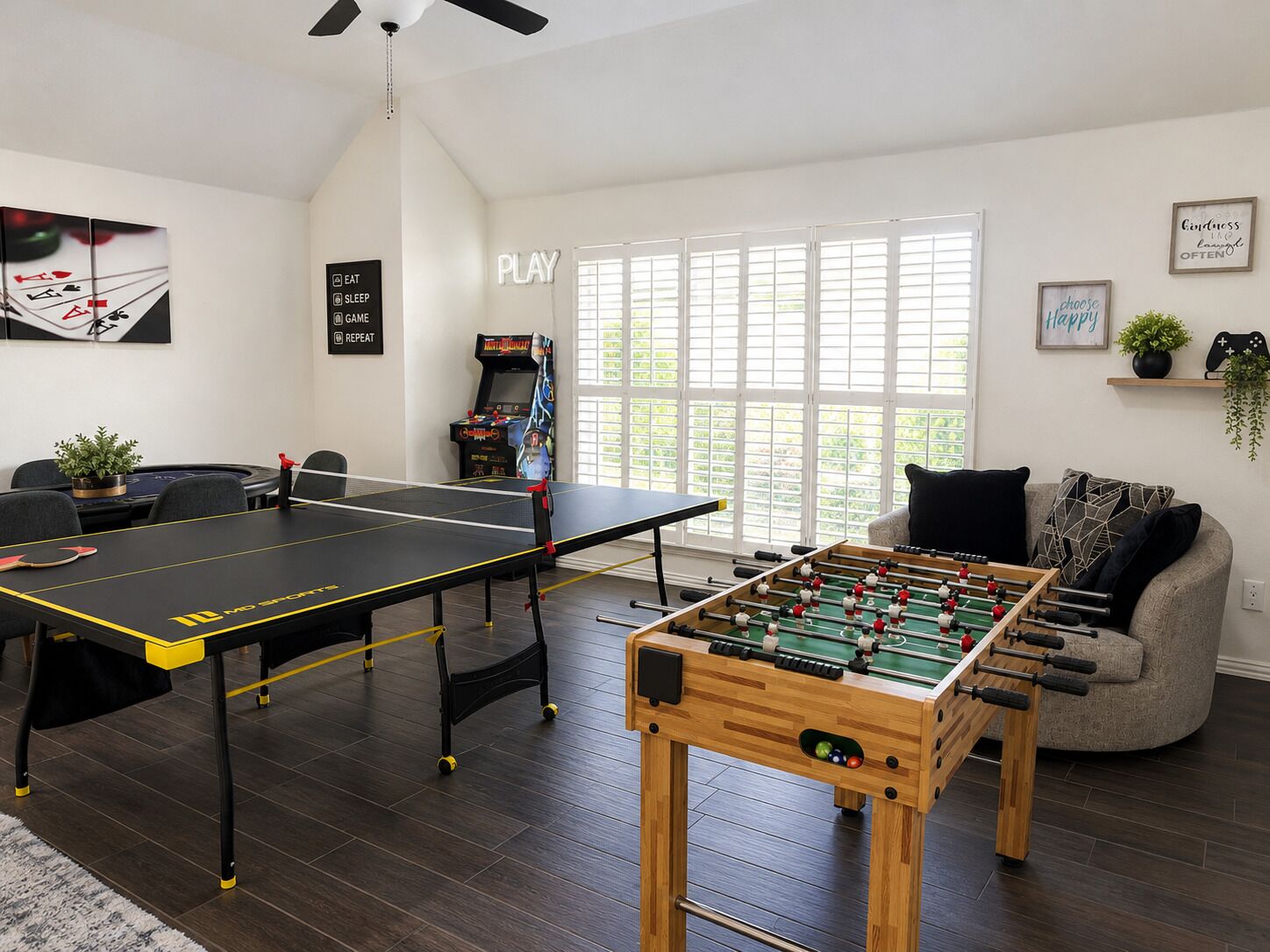 A room with a foosball table, a ping pong table, and a foosball table in the foreground.