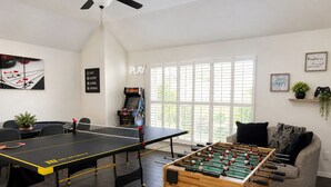 Una habitación con mesa de fútbol de mesa, mesa de ping pong y otra mesa de fútbol de mesa al frente.