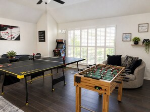 A room with a foosball table, a ping pong table, and a foosball table in the foreground.