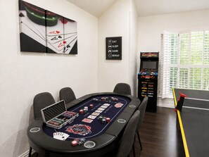 A poker table with chips and cards, a sign with options to eat, sleep, game, or repeat, and a video game machine.