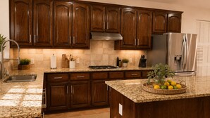 Una cocina con armarios de madera, un refrigerador de acero inoxidable, encimeras de granito y una isla central con fruteros.
